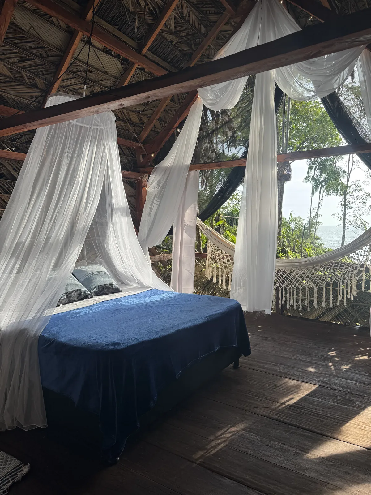 Cama del Glamping de LUX con mosquitero, cortinas y hamaca frente al mar